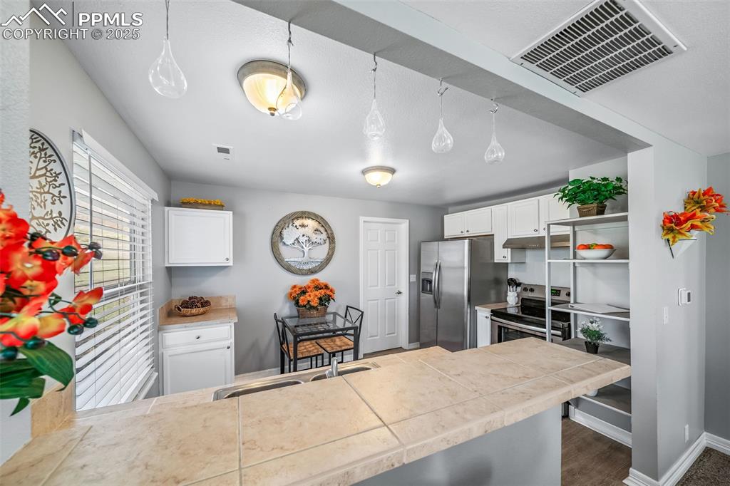Image 45 of 50: Kitchen with white cabinets, pendant lighting, stainless steel range with e
