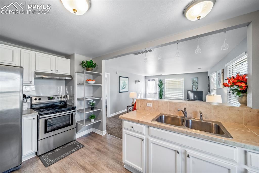 Image 46 of 50: Kitchen with white cabinets, stainless steel appliances, light wood-type fl