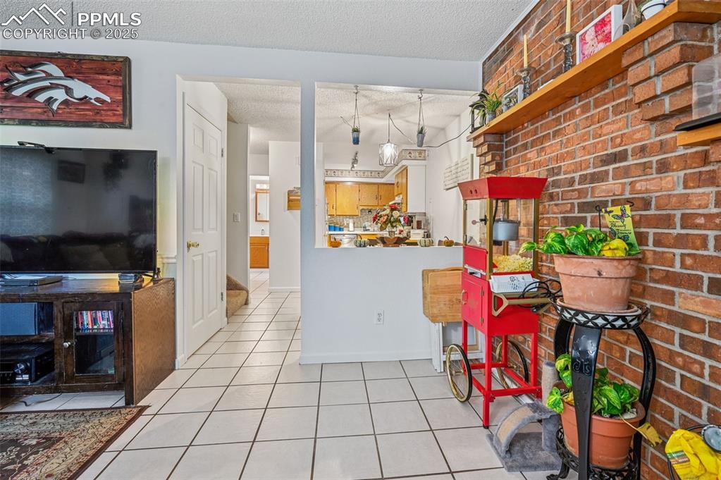 Image 4 of 21: Kitchen featuring brick wall, a textured ceiling, and light tile patterned 