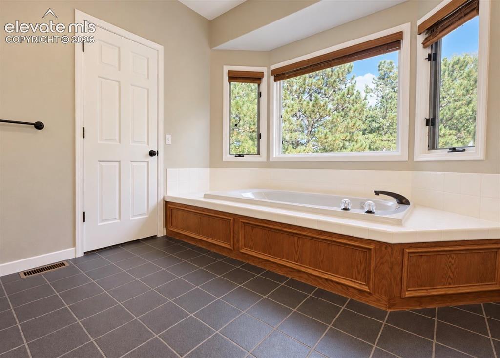 Image 8 of 8: Built-in soaking tub with a tiled surround, wood paneling, and a bay window