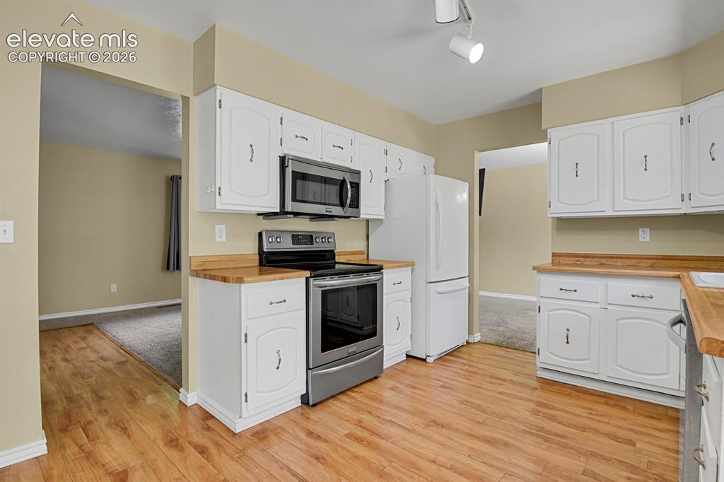 Image 11 of 34: Kitchen featuring wood-finish flooring, white cabinetry, stainless steel mi