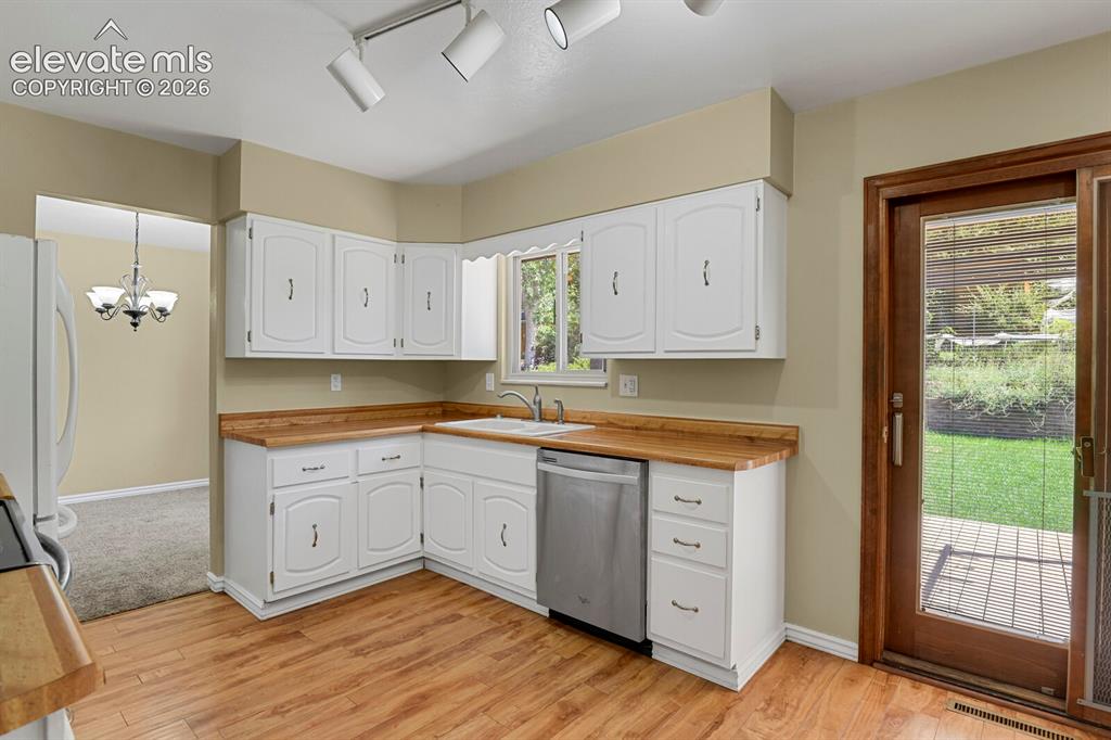 Image 12 of 34: White cabinetry with wood-finish countertops, stainless steel dishwasher, w