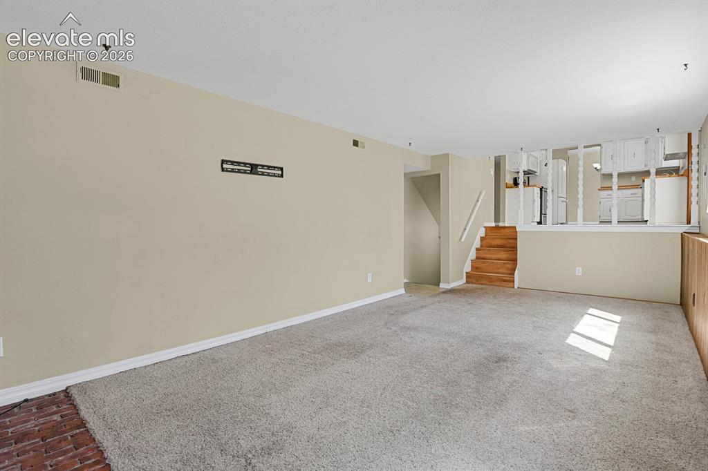 Image 21 of 34: Expansive carpeted living area with a partial brick-finish flooring accent