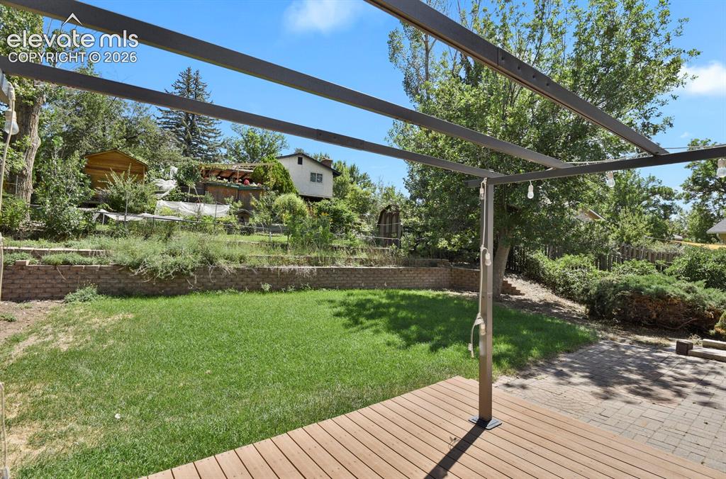 Image 27 of 34: Outdoor wood-finish deck with an overhead pergola structure, leading to a g