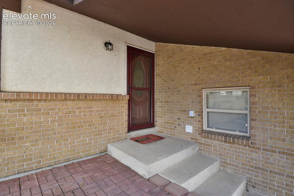 Image 3 of 34: Brick exterior with stucco accents, covered entry, concrete steps, and a re