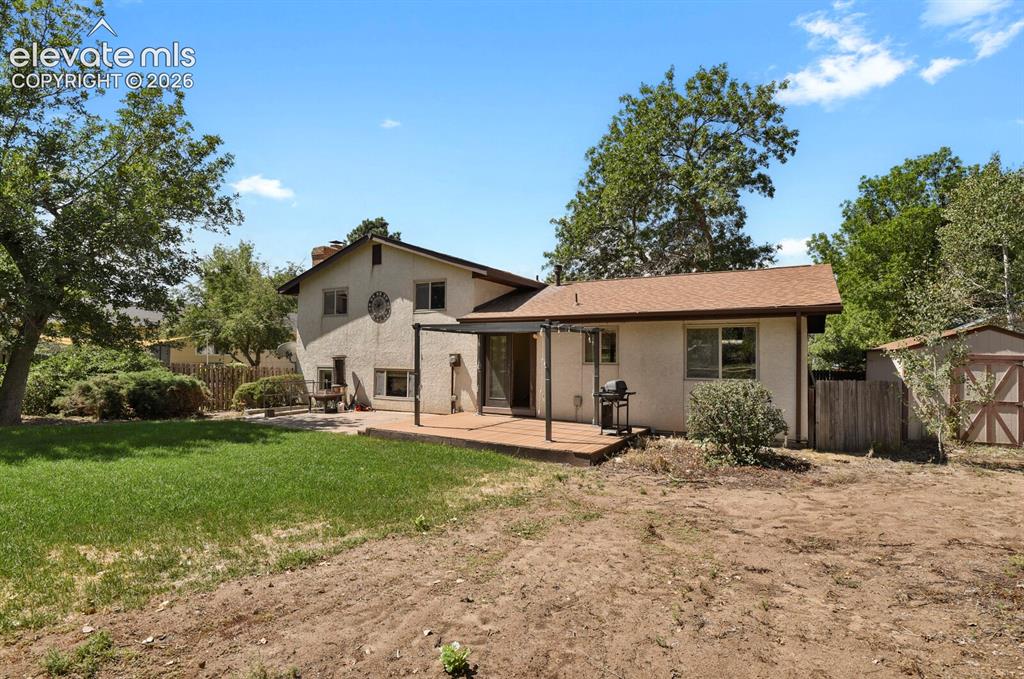 Image 30 of 34: Expansive backyard with a wood deck, partial covered patio, stucco exterior
