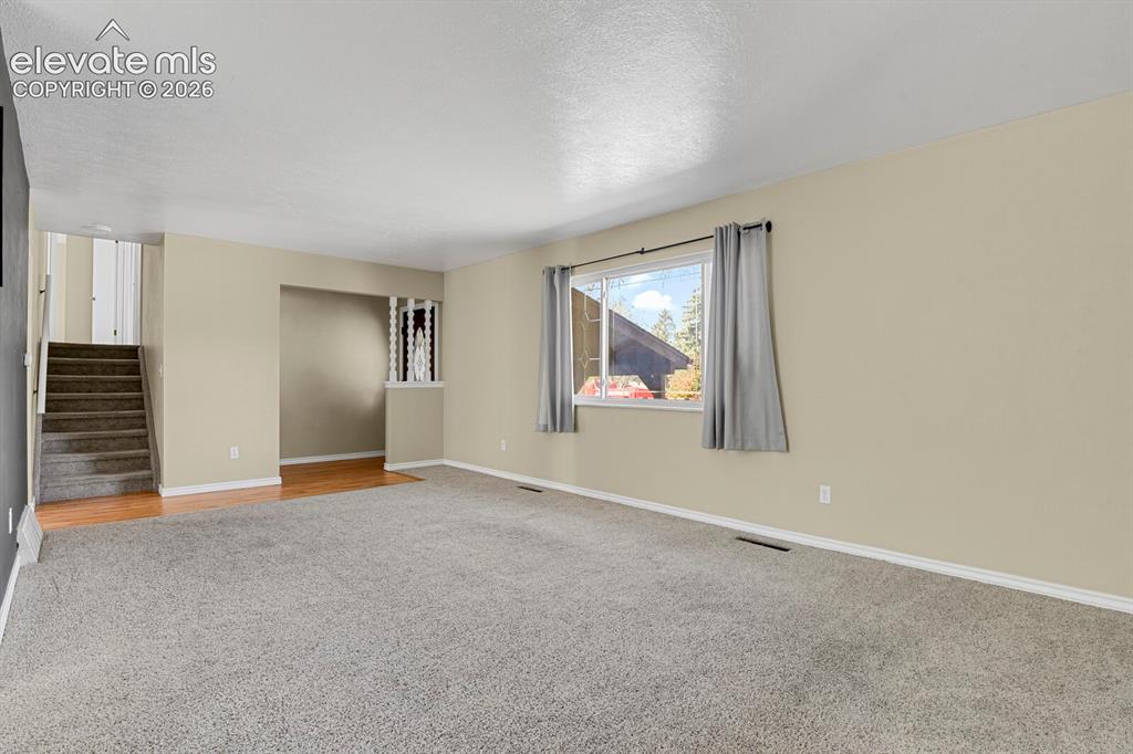 Image 6 of 34: Spacious living area featuring light-toned walls, grey carpet, a large wind