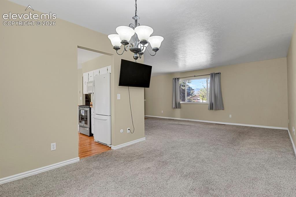 Image 7 of 34: Spacious carpeted living area with a large window, neutral wall tones, and
