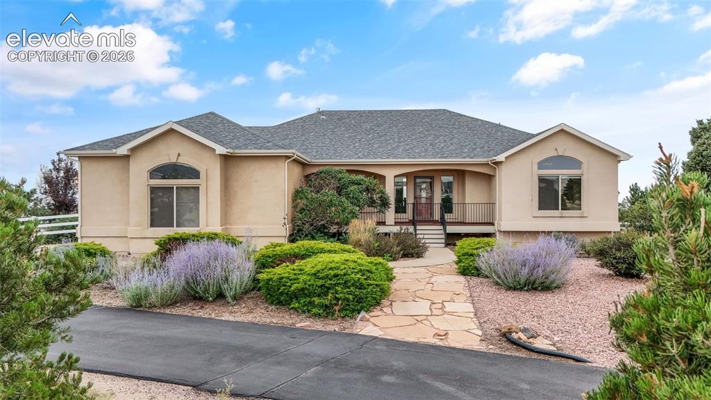 Caption: Stucco exterior with arched windows, flagstone walkway, mature landscaping, and an asphalt driveway