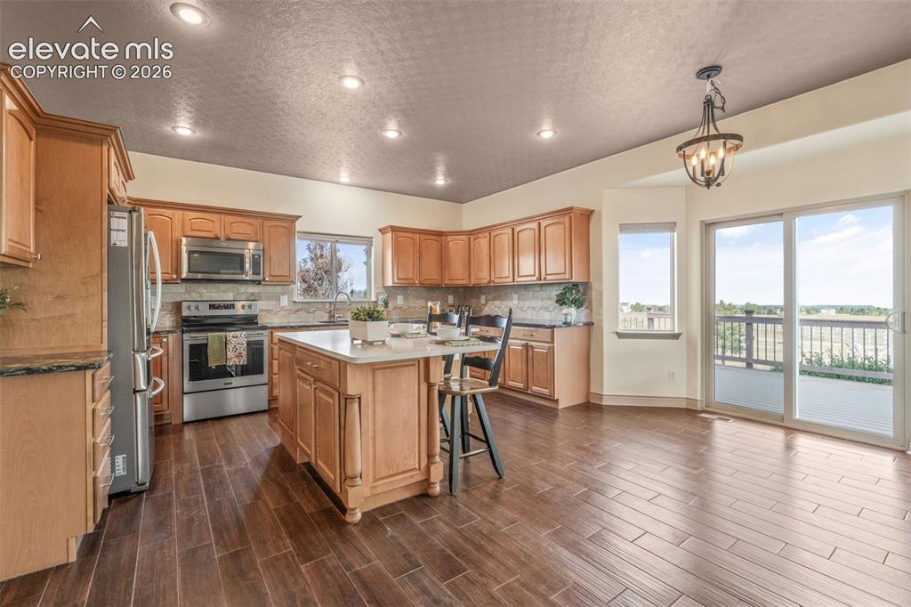 Image 11 of 49: Spacious kitchen featuring wood-finish flooring, light wood cabinetry, stai