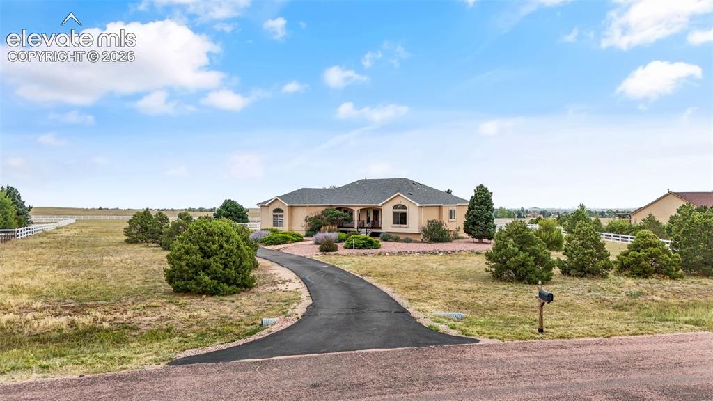 Image 2 of 49: Single-story residence featuring a paved driveway, mature landscaping, and