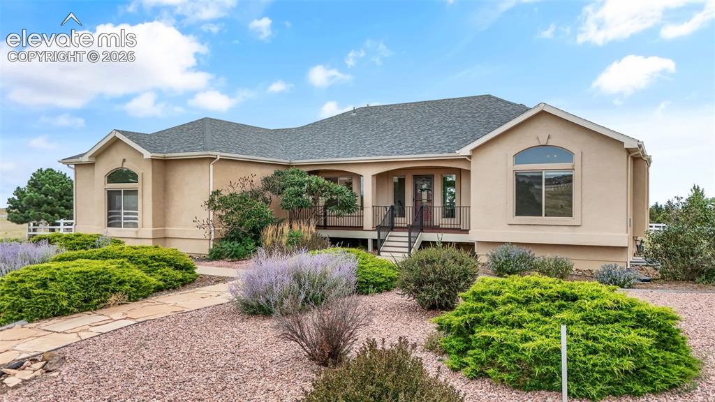 Image 4 of 49: Stucco exterior with a covered porch entry, arched windows, and a stone pat