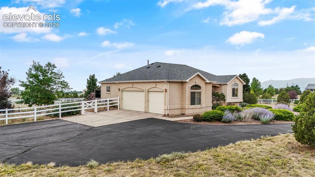 Image 42 of 49: Stucco exterior with a two-car garage and a wide driveway