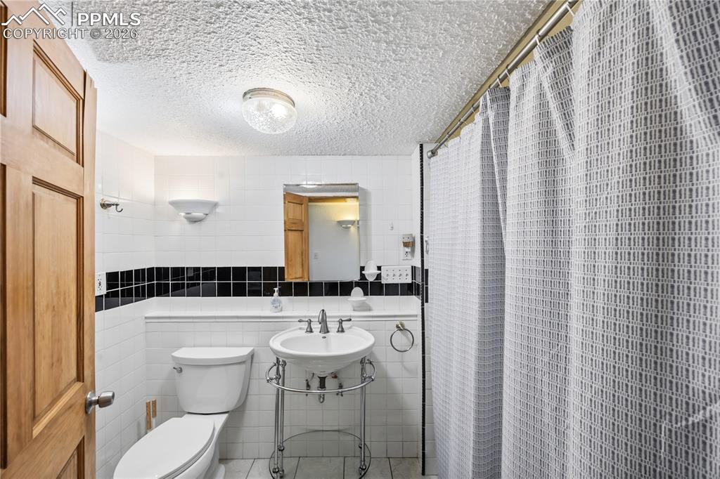 Image 32 of 47: Bathroom with tile walls, a shower with curtain, and a textured ceiling