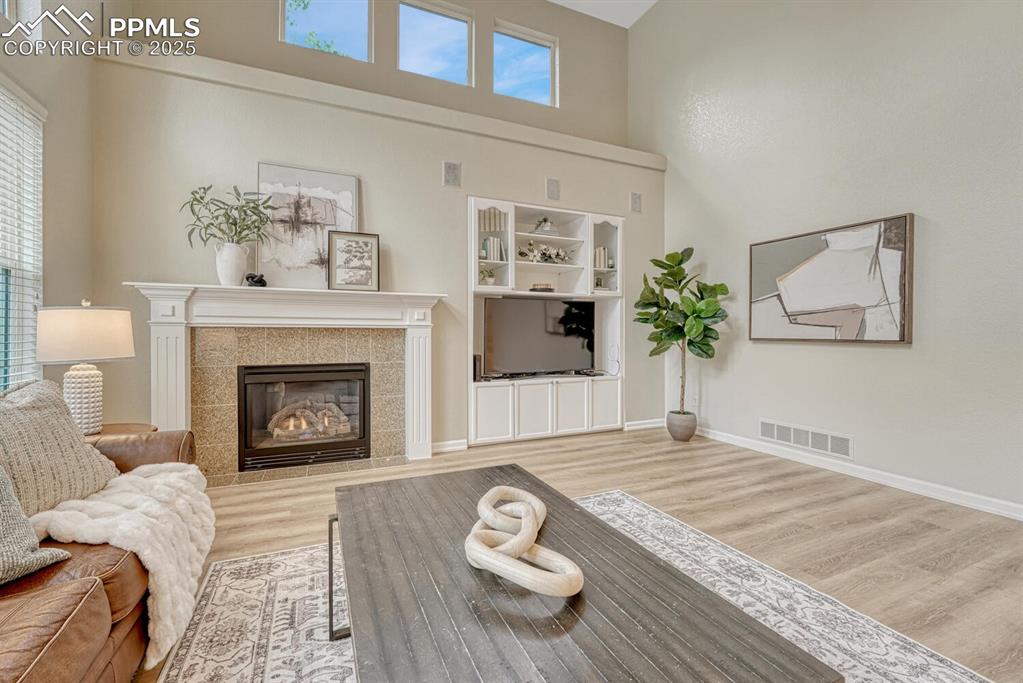 Image 19 of 50: Living room featuring a high ceiling, wood finished floors, and a fireplace