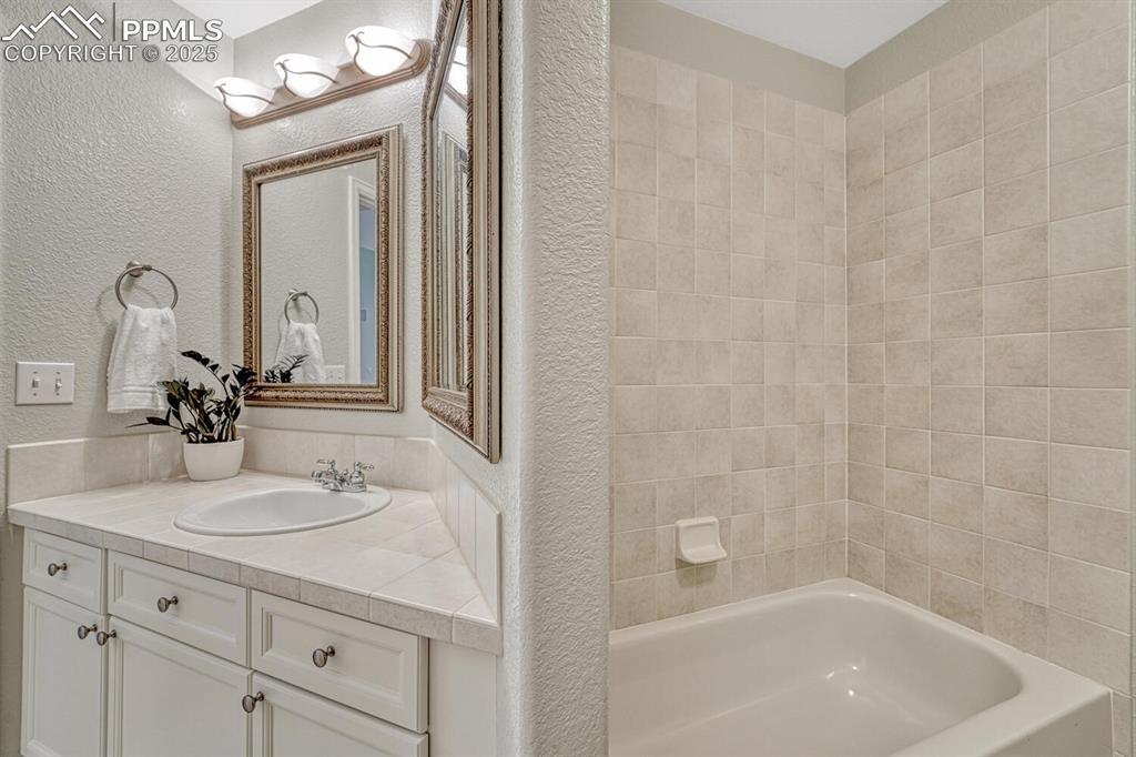 Image 22 of 50: Bathroom with a textured wall, vanity, and tub / shower combination