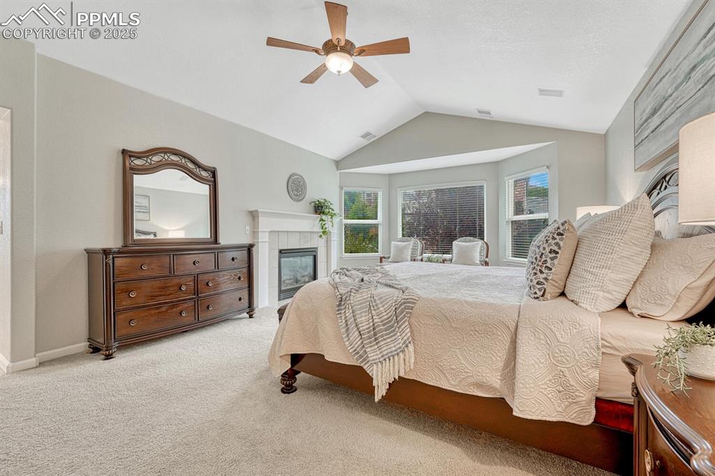 Image 23 of 50: Carpeted bedroom with vaulted ceiling, a tile fireplace, and ceiling fan