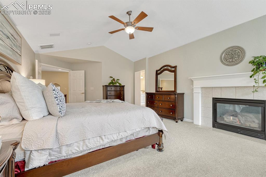 Image 24 of 50: Bedroom with lofted ceiling, carpet flooring, a tile fireplace, and a ceili