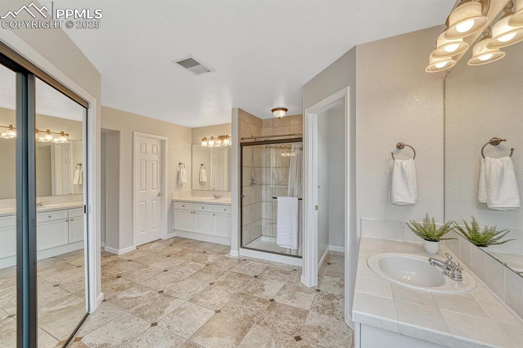 Image 28 of 50: Bathroom featuring a chandelier, a stall shower, and two vanities