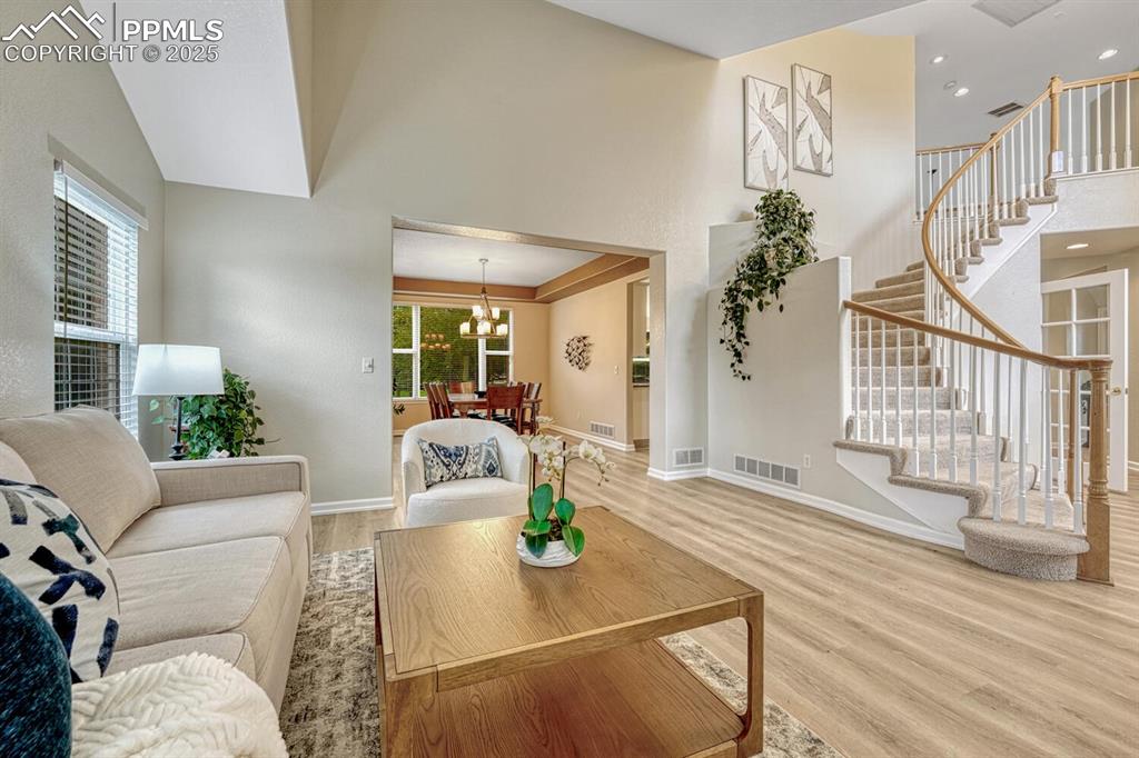 Image 3 of 50: Living area with wood finished floors, stairs, a chandelier, and a high cei