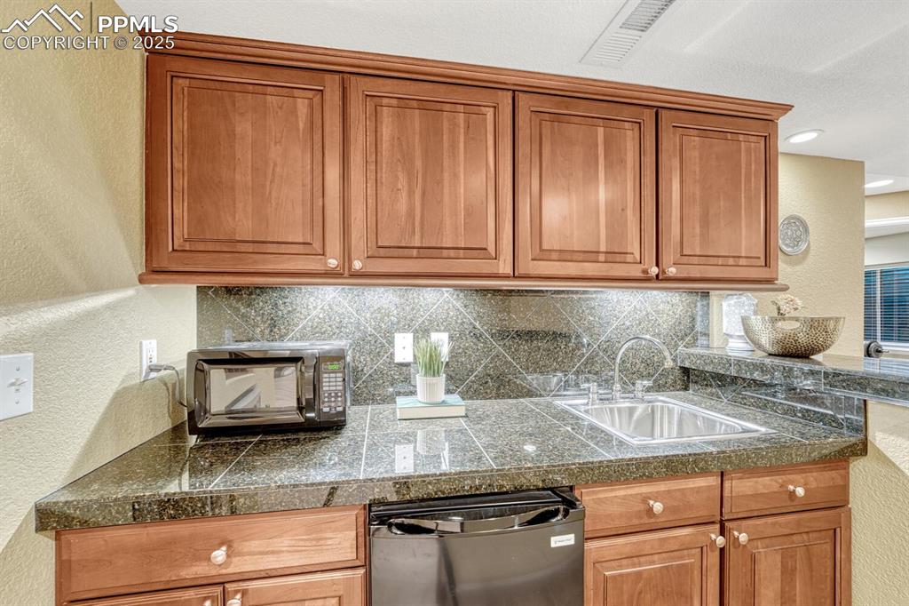 Image 39 of 50: Kitchen featuring tile countertops, a textured wall, brown cabinetry, black