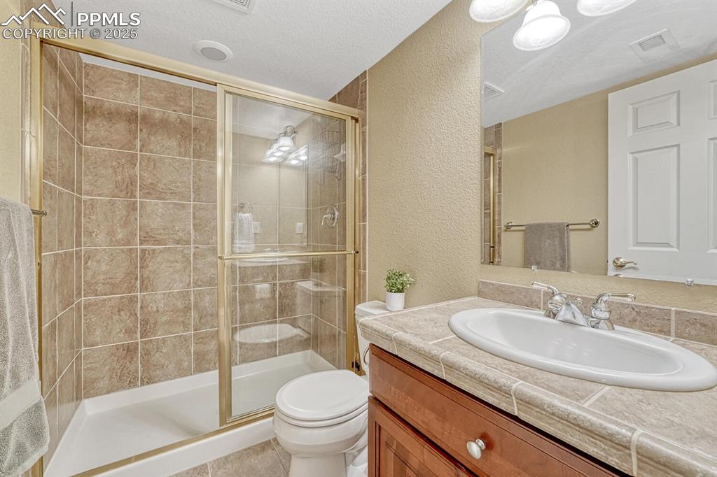 Image 43 of 50: Full bathroom featuring a textured wall, a shower stall, vanity, a textured