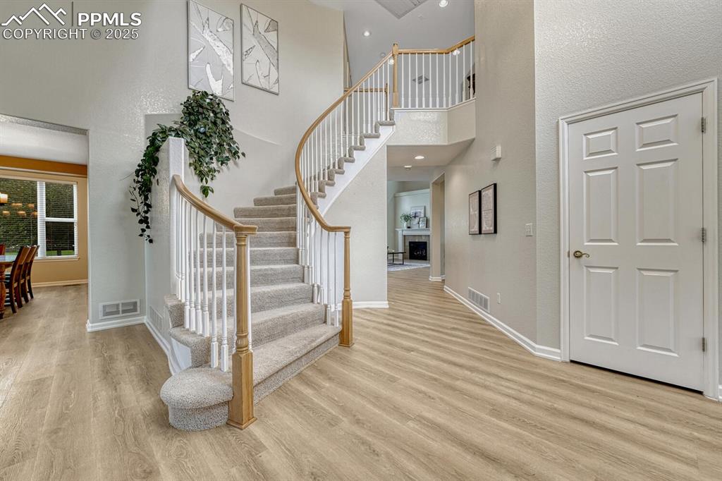 Image 8 of 50: Foyer with wood finished floors, stairs, a high ceiling, a fireplace, and r