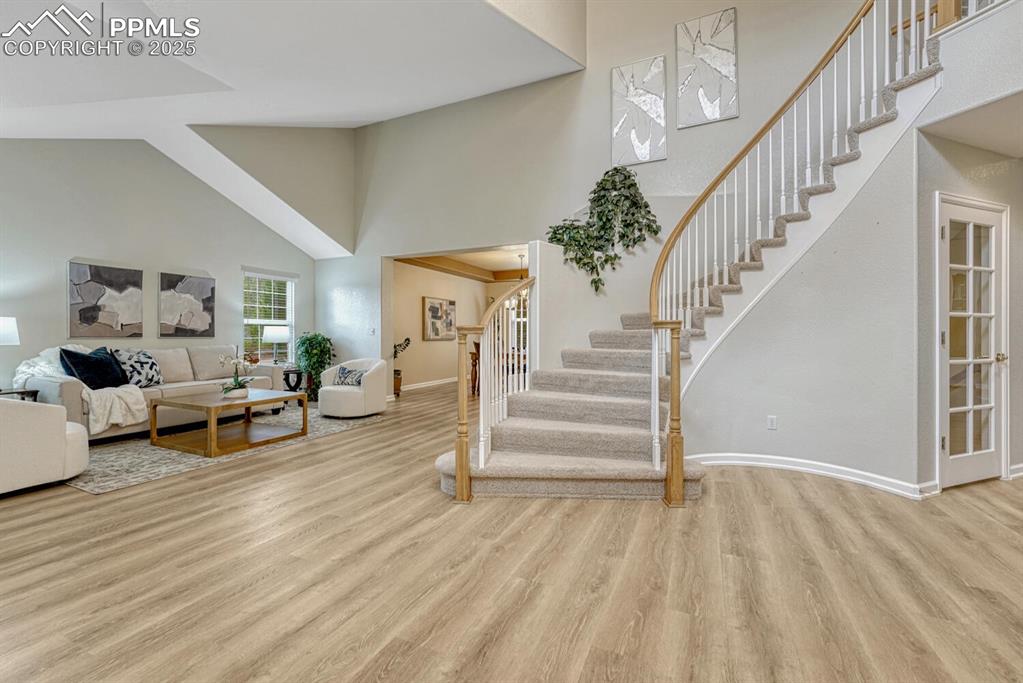 Image 9 of 50: Living room with high vaulted ceiling, stairway, and wood finished floors