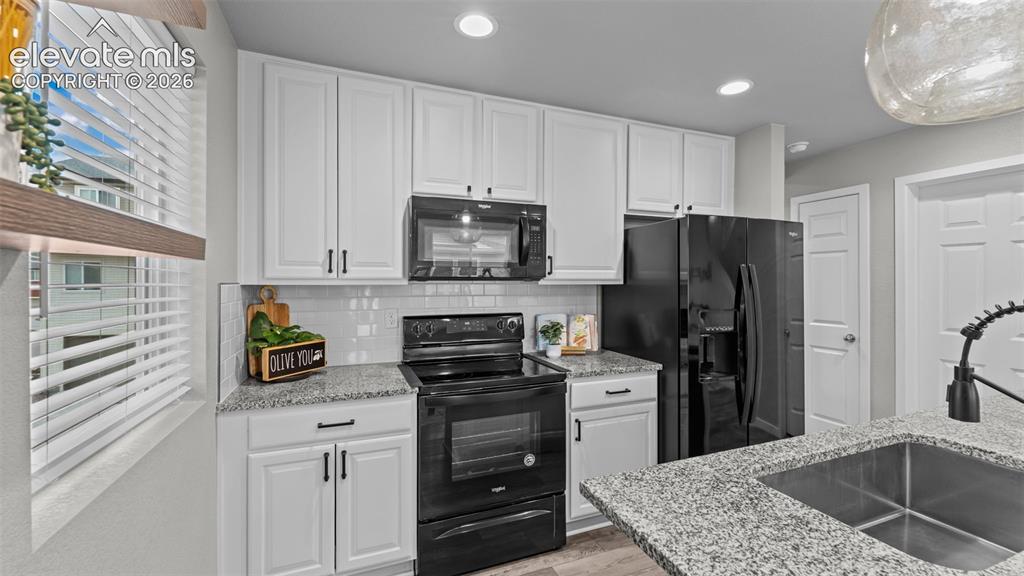 Image 14 of 34: Kitchen featuring white cabinetry, stone-finish countertops, subway tile ba