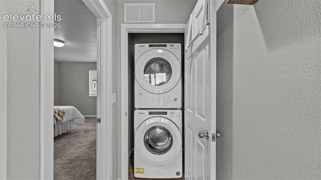 Image 23 of 34: Laundry closet featuring stacked front-load washer and dryer units and a si