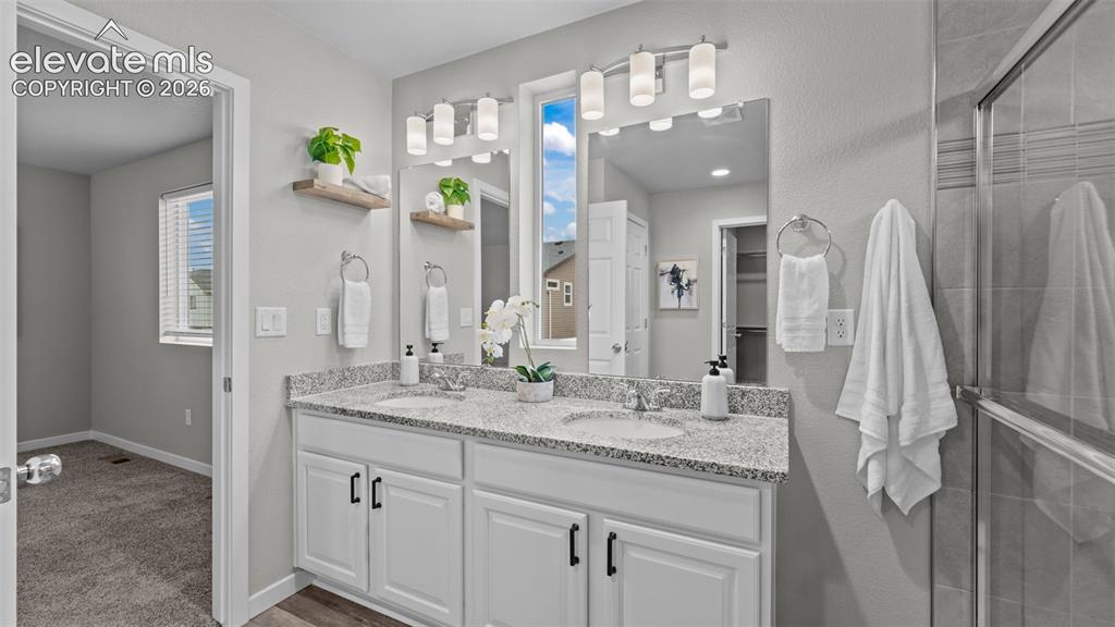 Image 28 of 34: Dual-sink vanity with stone-finish countertop, white shaker-style cabinetry