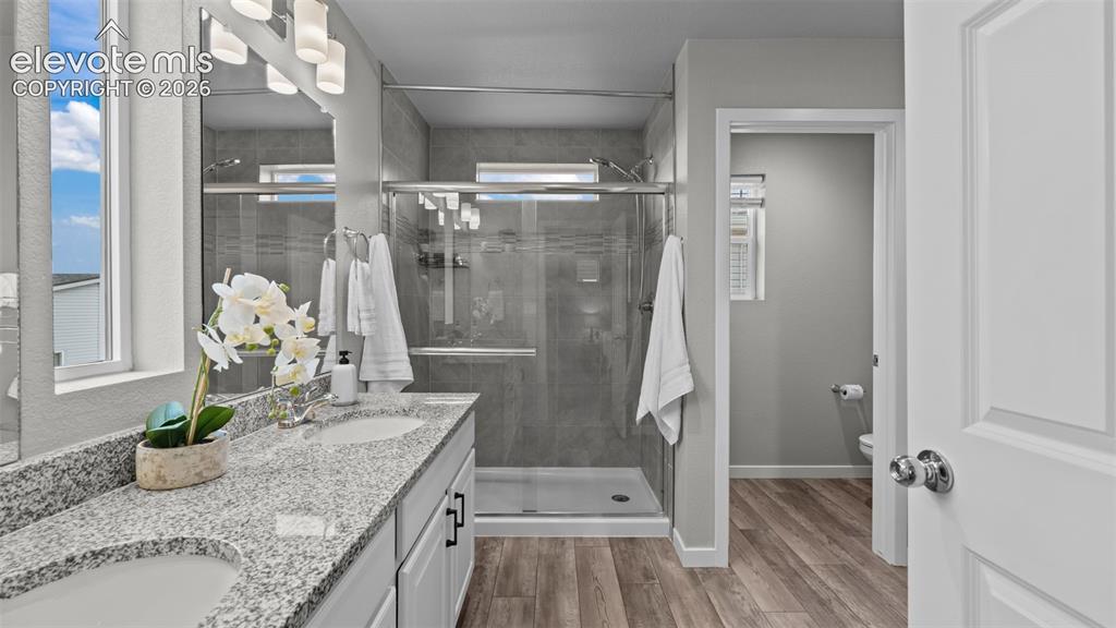 Image 29 of 34: Dual-sink vanity with stone-style countertops, walk-in shower featuring gla