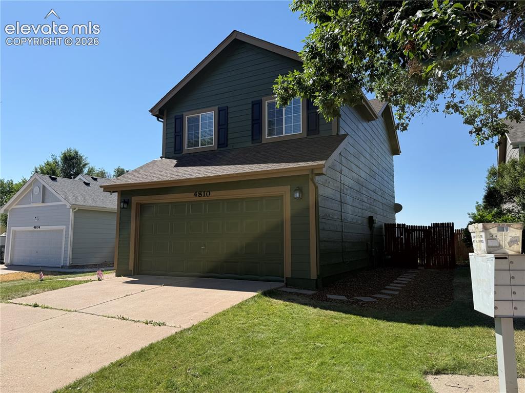Caption: Two-story residence featuring a two-car garage with overhead door, green siding, and a gabled roof