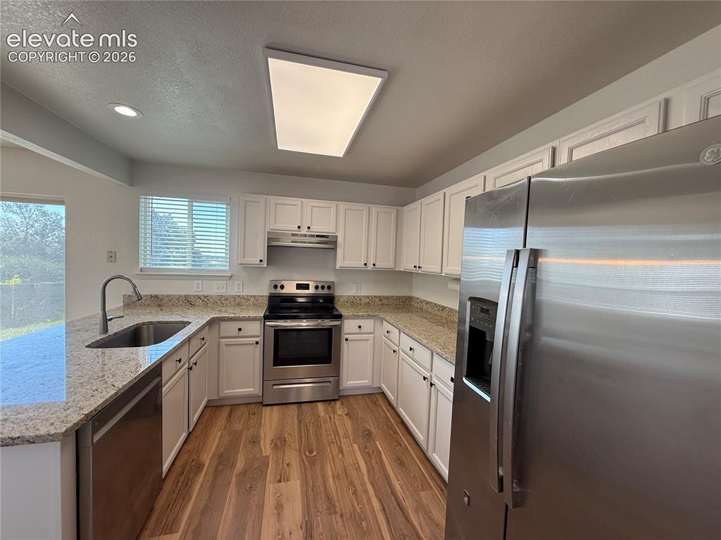 Image 11 of 20: Kitchen featuring wood-finish flooring, white cabinetry, speckled counterto