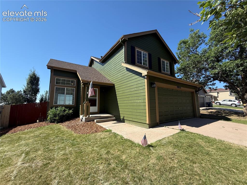Image 2 of 20: Two-story residence featuring green siding with contrasting trim, a two-car