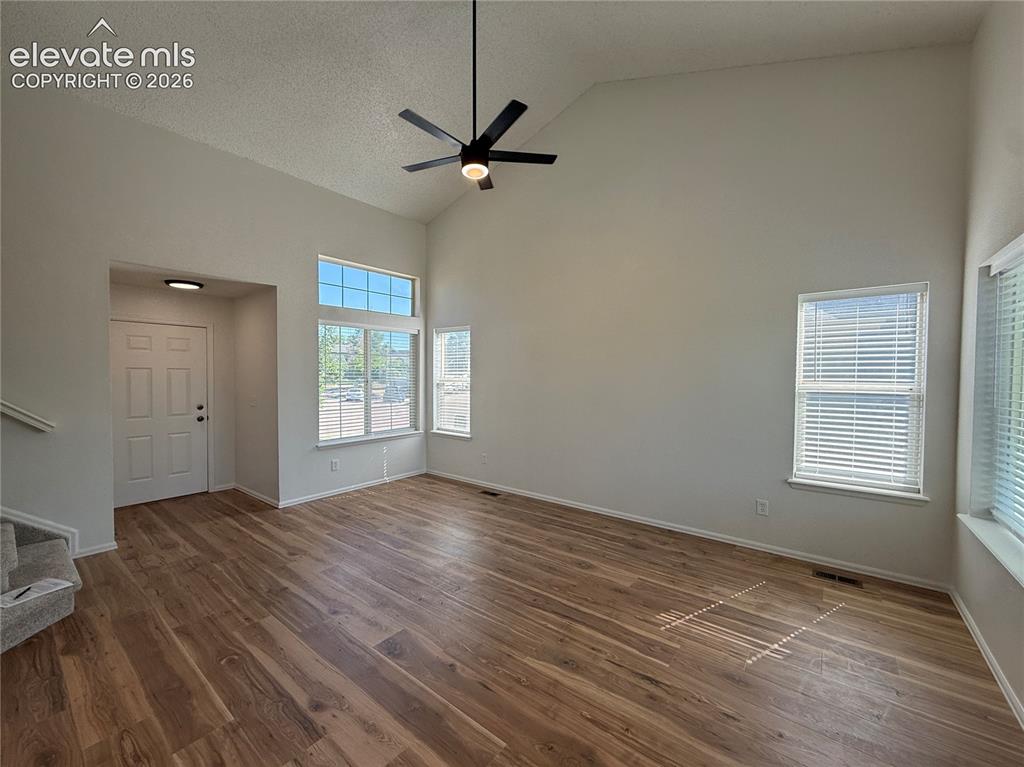 Image 7 of 20: Spacious living area featuring vaulted ceilings, wood-finish flooring, a co