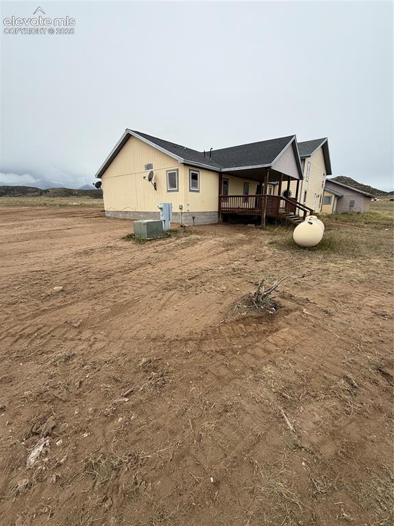 Image 18 of 19: Yellow-sided exterior with a covered wooden porch, dark shingled roof, and
