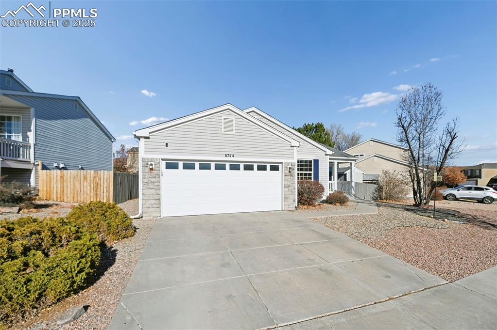 Caption: Ranch-style house featuring concrete driveway, stone siding, and a garage