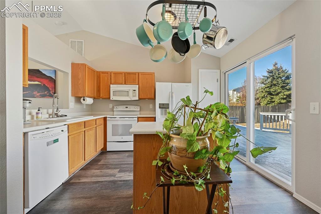 Image 11 of 24: Kitchen with vaulted ceiling, white appliances, light countertops, dark woo