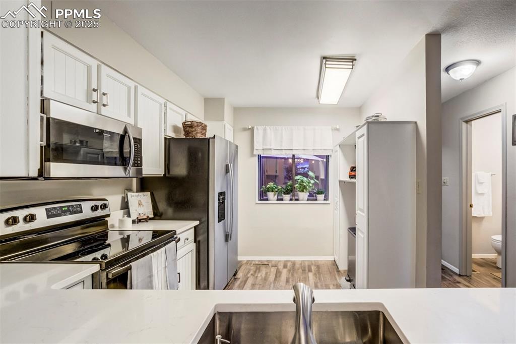 Image 12 of 31: Kitchen with stainless steel appliances, light wood-type flooring, white ca