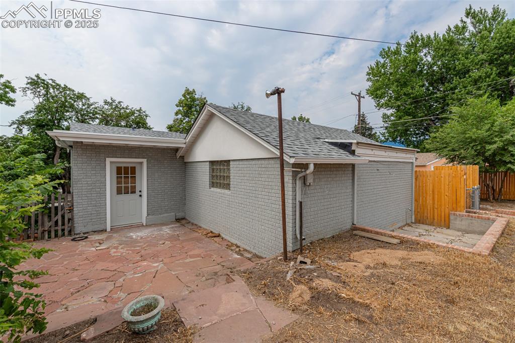 Image 32 of 35: View of side of property featuring a shingled roof, a patio, and brick sidi