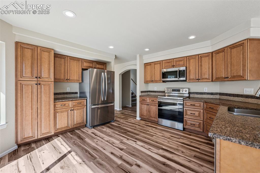 Image 2 of 43: Kitchen with a sink, brown cabinetry, arched walkways, and stainless steel