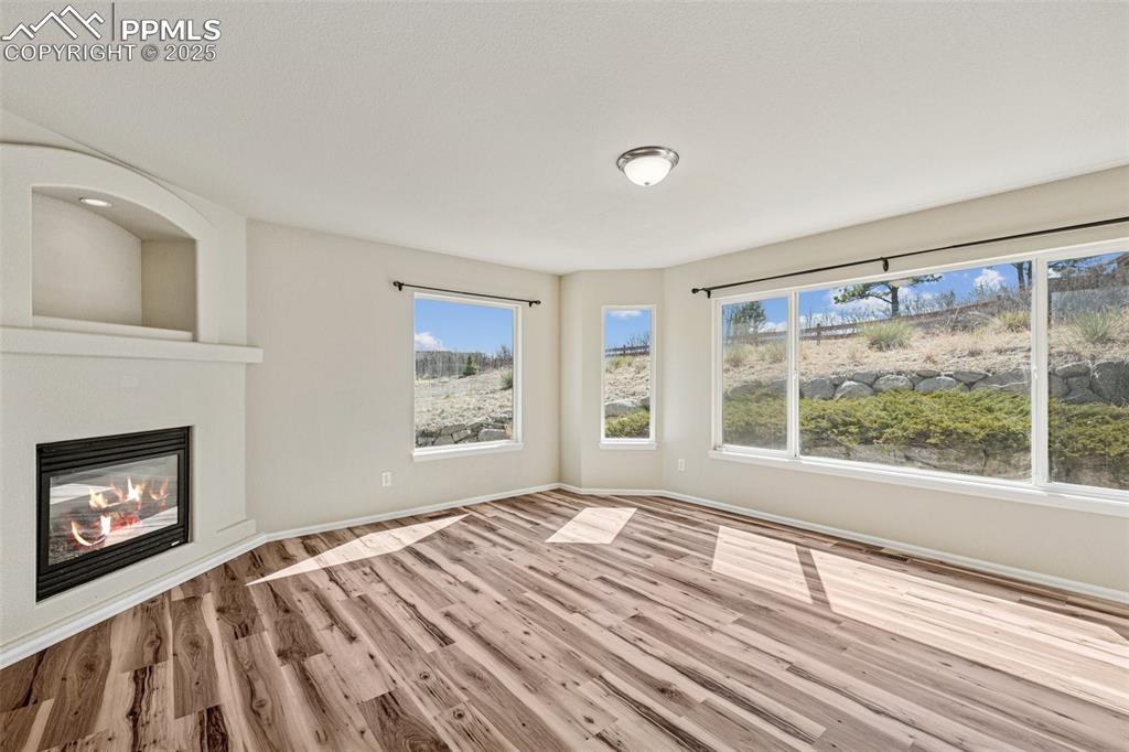 Image 23 of 43: Unfurnished living room featuring a glass covered fireplace, baseboards, pl