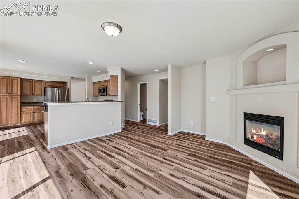 Image 24 of 43: Unfurnished living room with a glass covered fireplace, baseboards, wood fi