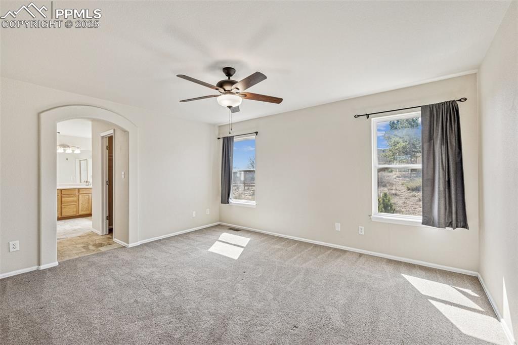 Image 27 of 43: Primary bedroom with a ceiling fan, baseboards, arched walkways, carpet flo