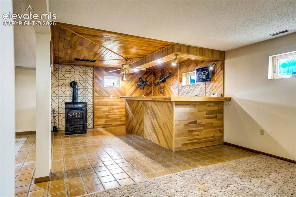 Image 29 of 48: wet bar, wood burning ceramic stove, tiled flooring