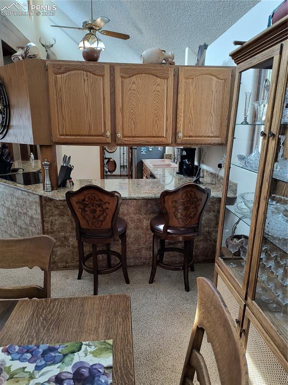 Image 11 of 50: Kitchen with a textured ceiling, brown cabinetry, a breakfast bar, ceiling