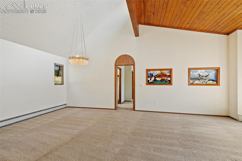 Image 22 of 50: Spare room featuring arched walkways, carpet floors, beam ceiling, high vau