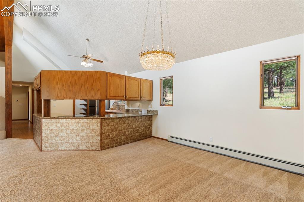 Image 23 of 50: Kitchen with vaulted ceiling, brown cabinets, a baseboard heating unit, a c