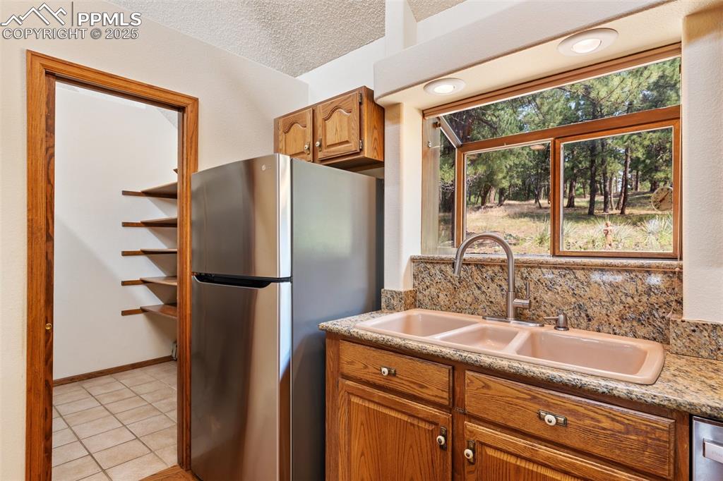 Image 28 of 50: Kitchen with a textured ceiling, freestanding refrigerator, brown cabinetry